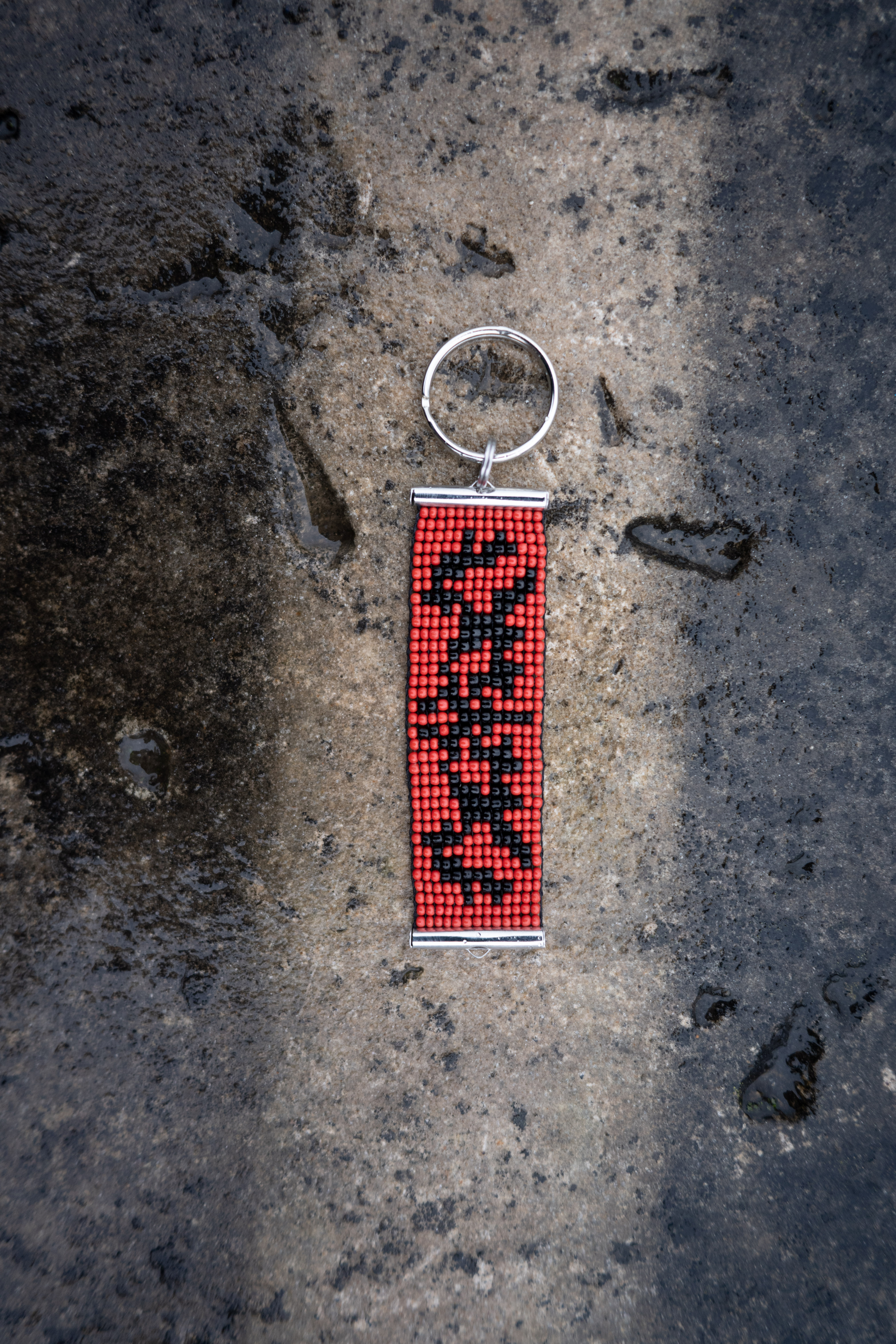 Red and black graphic beaded keyring photographed on wet concrete