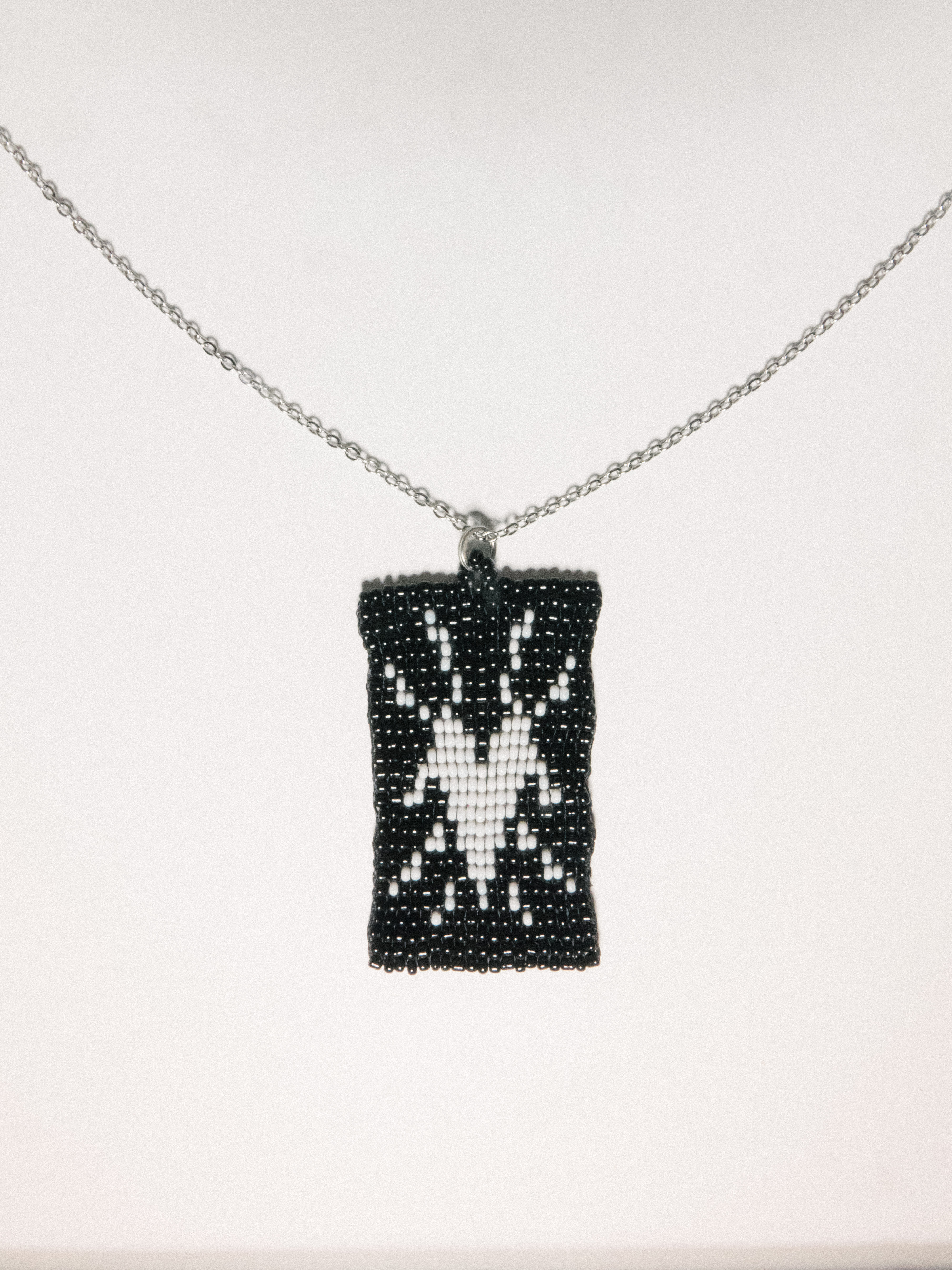 Black beaded pendant with a white spider motif on a silver chain