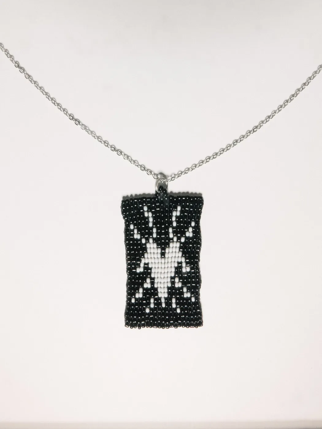Black beaded pendant with a white spider motif on a silver chain